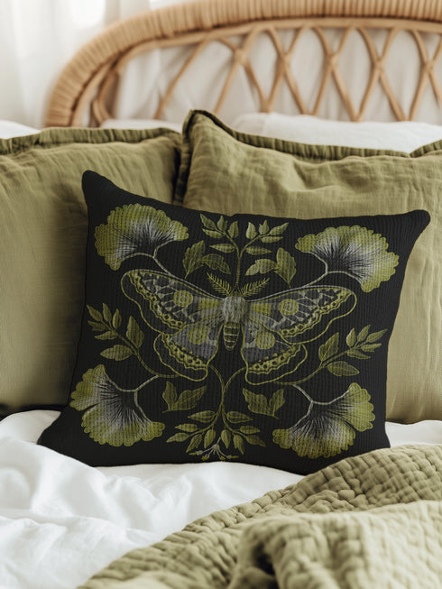 A square decorative pillow featuring an intricately detailed Luna moth in sage green and olive tones on a black background. The moth is centered in a symmetrical arrangement with ginkgo-like leaves and botanical elements surrounding it.